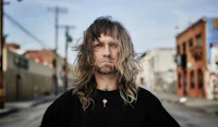 a man with long hair standing in a street