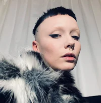 a woman with a shaved head wearing a fur coat